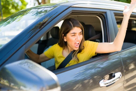 Angry driver with road rage sticks her hand out the window in frustration on a sunny day
