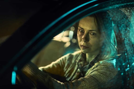 Woman looks out her car window while driving at night with a worried look on her face